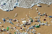 A very idyllic sandy beach is covered in plastic waste, right at the sea shore